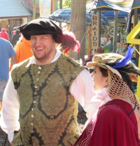 A man and woman in Renaissance clothing stand together laughing at a Renaissance faire