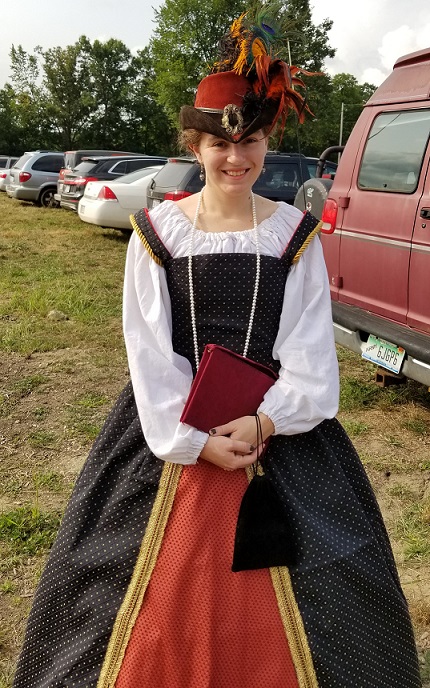 A woman in in a Renaissance gown stands smiling in a parking lot